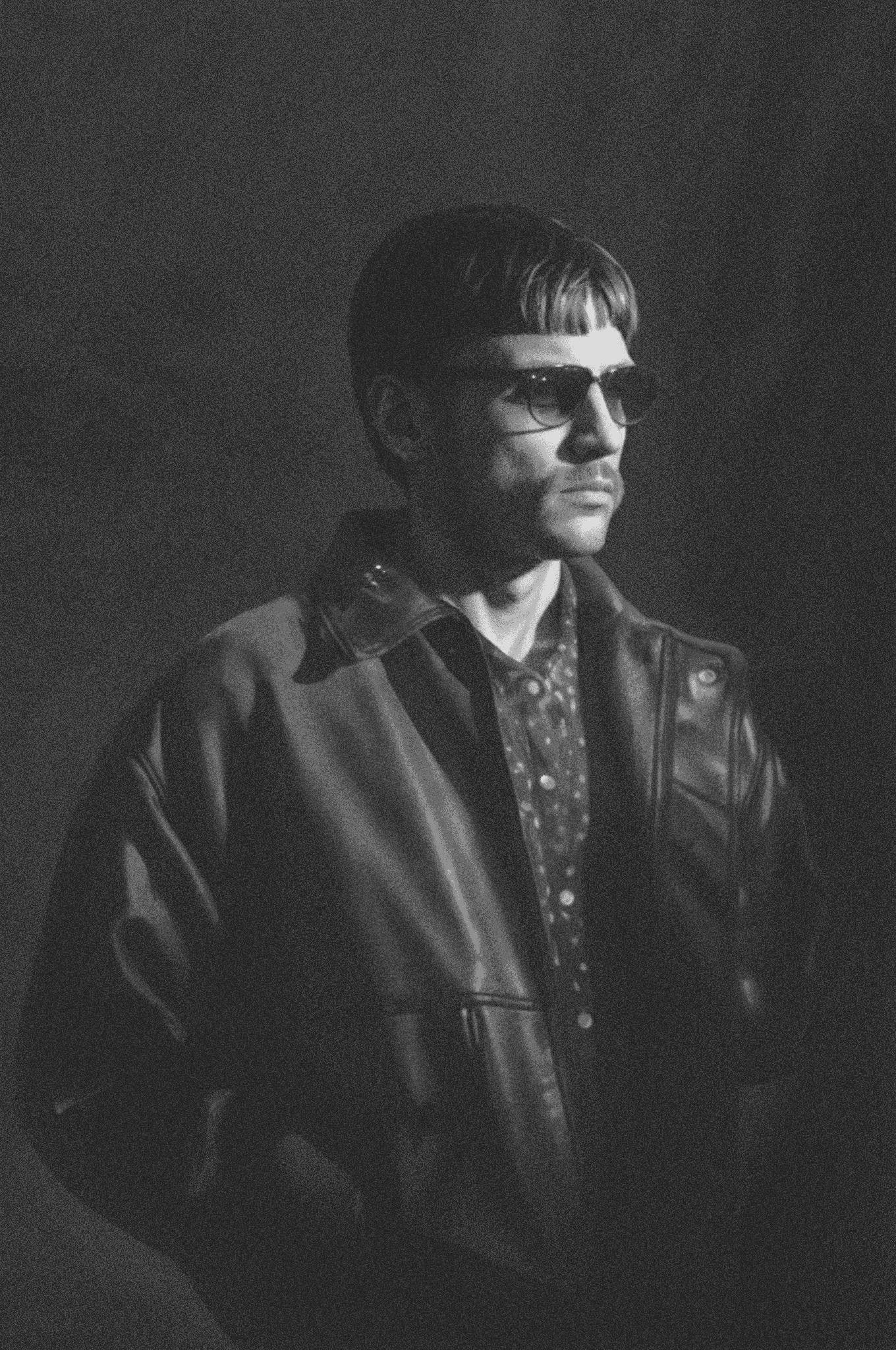 Sasha Piankov in sunglasses and a leather jacket, the complete vertical black-and-white portrait